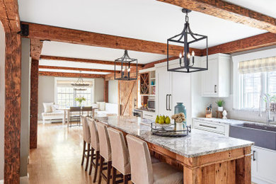 Example of a large cottage l-shaped light wood floor and exposed beam eat-in kitchen design in Portland Maine with paneled appliances, a farmhouse sink, shaker cabinets, white cabinets, white backsplash, subway tile backsplash, an island, granite countertops and multicolored countertops