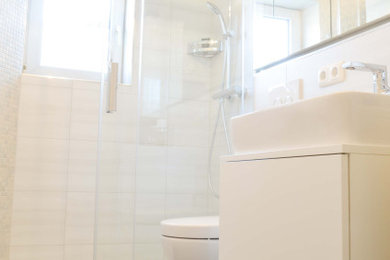 Modernes Duschbad mit weißen Schränken, offener Dusche, Wandtoilette, weißen Fliesen, beiger Wandfarbe, dunklem Holzboden, Unterbauwaschbecken, braunem Boden, Schiebetür-Duschabtrennung und weißer Waschtischplatte in München