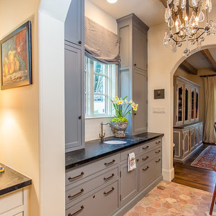 ヒューストンの中サイズの地中海スタイルのおしゃれなウェットバー (アンダーカウンターシンク、家具調キャビネット、青いキャビネット、ソープストーンカウンター、ベージュキッチンパネル、サブウェイタイルのキッチンパネル、テラコッタタイルの床) の写真