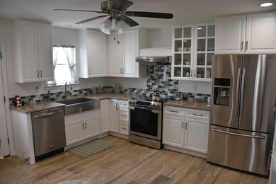 Open concept kitchen - mid-sized traditional l-shaped medium tone wood floor and brown floor open concept kitchen idea in New York with a farmhouse sink, raised-panel cabinets, white cabinets, granite countertops, gray backsplash, ceramic backsplash, stainless steel appliances and no island