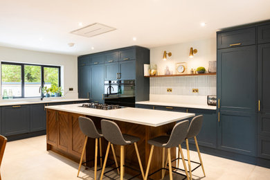 Photo of a medium sized classic open plan kitchen in Surrey with shaker cabinets, blue cabinets, quartz worktops, white splashback, cement tile splashback and white worktops.