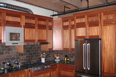 Mid-sized elegant l-shaped enclosed kitchen photo in Seattle with flat-panel cabinets, medium tone wood cabinets, granite countertops, stone tile backsplash, stainless steel appliances, an island and gray backsplash