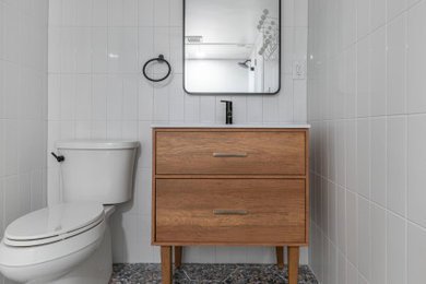 Photo of a medium sized retro bathroom in DC Metro with freestanding cabinets, medium wood cabinets, a two-piece toilet, white tiles, porcelain tiles, white walls, porcelain flooring, an integrated sink, green floors, a freestanding vanity unit, an alcove shower, an open shower and a wall niche.