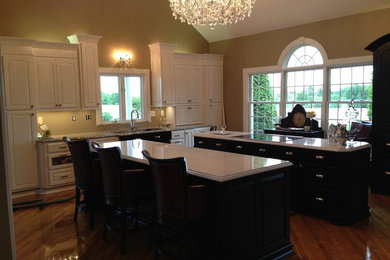 Large elegant u-shaped medium tone wood floor open concept kitchen photo in Other with a double-bowl sink, white cabinets, marble countertops, stainless steel appliances, two islands and raised-panel cabinets