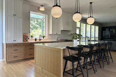 Example of a large transitional l-shaped light wood floor and brown floor open concept kitchen design in Portland with an undermount sink, shaker cabinets, medium tone wood cabinets, quartzite countertops, white backsplash, ceramic backsplash, stainless steel appliances, an island and beige countertops