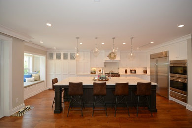 Inspiration for a large transitional medium tone wood floor and brown floor kitchen remodel in Miami with a double-bowl sink, shaker cabinets, white cabinets, quartzite countertops, white backsplash, glass tile backsplash, stainless steel appliances and an island