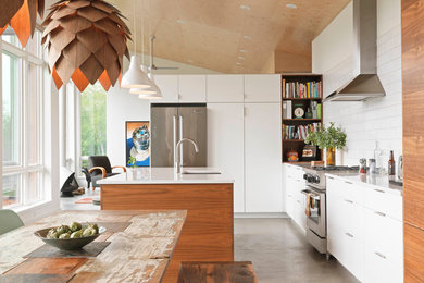 Trendy l-shaped concrete floor and gray floor open concept kitchen photo in Burlington with an undermount sink, flat-panel cabinets, white cabinets, white backsplash, subway tile backsplash, stainless steel appliances and an island