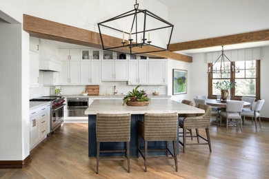Mid-sized elegant l-shaped medium tone wood floor, brown floor and exposed beam eat-in kitchen photo in Denver with an undermount sink, shaker cabinets, white cabinets, white backsplash, subway tile backsplash, stainless steel appliances, an island and white countertops