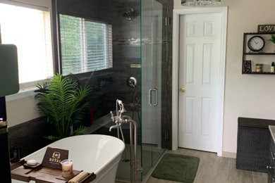 This is an example of a mid-sized transitional master bathroom in Denver with raised-panel cabinets, black cabinets, a freestanding tub, a corner shower, gray tile, porcelain tile, beige walls, porcelain floors, an undermount sink, beige floor, a hinged shower door and beige benchtops.