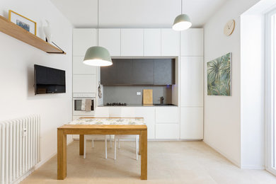 This is an example of a beach style single-wall eat-in kitchen in Rome with a drop-in sink, flat-panel cabinets, white cabinets, grey splashback, white appliances and beige floor.