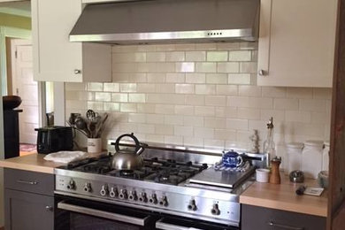 Example of a mountain style medium tone wood floor and brown floor open concept kitchen design in New York with shaker cabinets, black cabinets, wood countertops, white backsplash, ceramic backsplash, stainless steel appliances and brown countertops