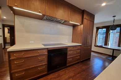 Example of a transitional galley medium tone wood floor and brown floor eat-in kitchen design in Los Angeles with recessed-panel cabinets, medium tone wood cabinets, white countertops, quartz countertops, white backsplash, porcelain backsplash, black appliances and an island