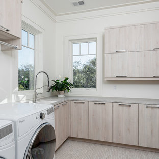 チャールストンの中サイズのコンテンポラリースタイルのおしゃれな洗濯室 (アンダーカウンターシンク、フラットパネル扉のキャビネット、淡色木目調キャビネット、白い壁、左右配置の洗濯機・乾燥機、ベージュの床、グレーのキッチンカウンター、珪岩カウンター、磁器タイルの床) の写真
