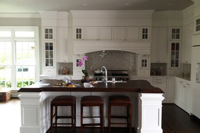 Inspiration for a large contemporary u-shaped dark wood floor eat-in kitchen remodel in Raleigh with an undermount sink, glass-front cabinets, white cabinets, granite countertops, beige backsplash, stone tile backsplash, stainless steel appliances and an island