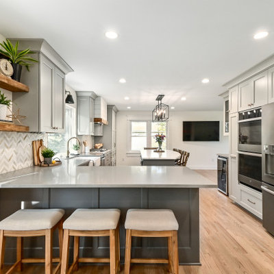 Huge farmhouse l-shaped medium tone wood floor and brown floor eat-in kitchen photo in Milwaukee with a farmhouse sink, shaker cabinets, gray cabinets, quartz countertops, white backsplash, marble backsplash, stainless steel appliances, an island and gray countertops