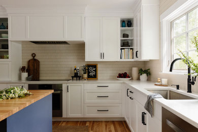 Inspiration for a large contemporary l-shaped medium tone wood floor kitchen remodel in Boston with an undermount sink, shaker cabinets, white cabinets, quartz countertops, white backsplash, ceramic backsplash, black appliances, an island and white countertops