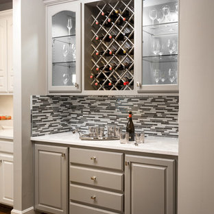 カンザスシティの小さいトランジショナルスタイルのおしゃれなウェットバー (レイズドパネル扉のキャビネット、グレーのキャビネット、クオーツストーンカウンター、グレーのキッチンパネル、ガラス板のキッチンパネル、シンクなし、無垢フローリング、白いキッチンカウンター) の写真