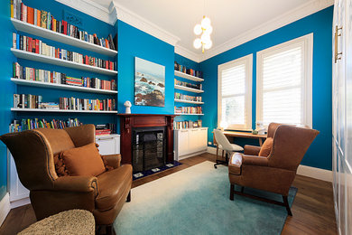 Small transitional guest bedroom in Sydney with blue walls, medium hardwood floors, a standard fireplace, a wood fireplace surround and brown floor.