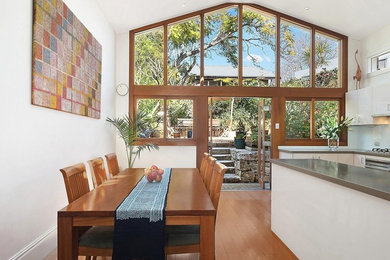 Photo of a mid-sized traditional galley eat-in kitchen in Sydney with flat-panel cabinets, white cabinets, quartz benchtops, blue splashback, glass sheet splashback, medium hardwood floors, with island and grey benchtop.