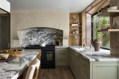 Inspiration for a large transitional l-shaped medium tone wood floor and brown floor kitchen remodel in Sacramento with an undermount sink, shaker cabinets, green cabinets, marble countertops, white backsplash, stone slab backsplash, black appliances, an island and white countertops