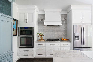Mid-sized farmhouse u-shaped medium tone wood floor and brown floor kitchen pantry photo in Atlanta with a farmhouse sink, shaker cabinets, white cabinets, quartzite countertops, gray backsplash, ceramic backsplash, stainless steel appliances, an island and gray countertops