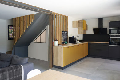 Cette image montre une cuisine design avec des portes de placard jaunes, un plan de travail en bois, une crédence noire, un électroménager noir et un sol gris.