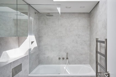 This is an example of a mid-sized contemporary kids bathroom in London with a drop-in tub, a shower/bathtub combo, a one-piece toilet, gray tile, a wall-mount sink and tile benchtops.