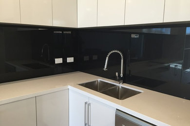 Inspiration for a contemporary kitchen in Adelaide with a double-bowl sink, flat-panel cabinets, white cabinets, engineered stone countertops, black splashback, glass sheet splashback and stainless steel appliances.