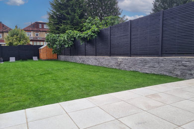 Medium sized modern back formal full sun garden in London with natural stone paving and a wood fence.