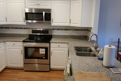 Inspiration for a mid-sized timeless l-shaped medium tone wood floor enclosed kitchen remodel in Other with an undermount sink, raised-panel cabinets, white cabinets, laminate countertops, white backsplash, stone tile backsplash, stainless steel appliances and a peninsula