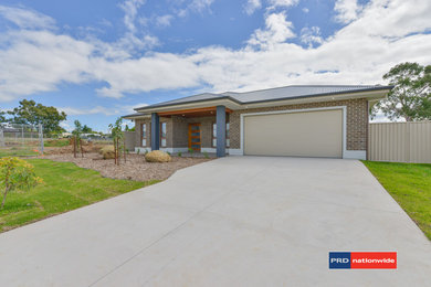 This is an example of a large contemporary one-storey brick brown house exterior in Newcastle - Maitland with a gable roof and a metal roof.
