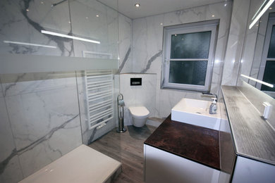 This is an example of a mid-sized contemporary 3/4 bathroom in Frankfurt with white cabinets, an alcove shower, a wall-mount toilet, white tile, ceramic tile, ceramic floors, a vessel sink, brown floor, an open shower and brown benchtops.