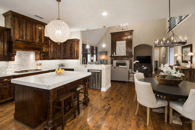 Inspiration for a large transitional u-shaped medium tone wood floor and brown floor eat-in kitchen remodel in Dallas with a farmhouse sink, raised-panel cabinets, dark wood cabinets, quartz countertops, gray backsplash, marble backsplash, stainless steel appliances, an island and white countertops