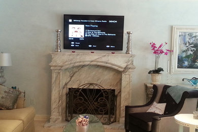 Photo of a traditional living room in New Orleans with a wall-mounted tv, white walls, light hardwood floors, a standard fireplace and a plaster fireplace surround.