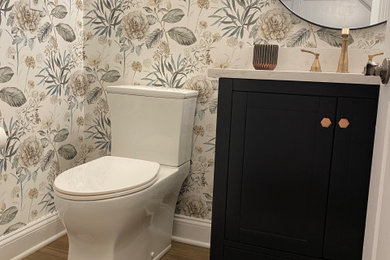 Inspiration for a small transitional ceramic tile, brown floor and wallpaper powder room remodel in New York with shaker cabinets, black cabinets, a two-piece toilet, multicolored walls, an undermount sink, quartz countertops, beige countertops and a freestanding vanity