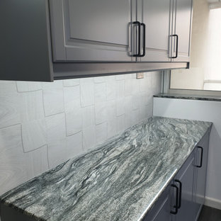 Foto på ett mellanstort funkis svart kök, med en nedsänkt diskho, luckor med lamellpanel, grå skåp, marmorbänkskiva, grått stänkskydd, stänkskydd i keramik, svarta vitvaror, vinylgolv och brunt golv