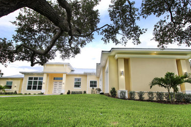 Photo of a large tropical one-storey yellow house exterior in Orlando with a hip roof and a metal roof.