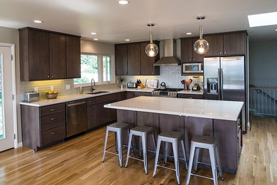 Mid-sized transitional l-shaped open plan kitchen in Salt Lake City with an undermount sink, flat-panel cabinets, dark wood cabinets, quartzite benchtops, white splashback, subway tile splashback, stainless steel appliances, light hardwood floors and with island.