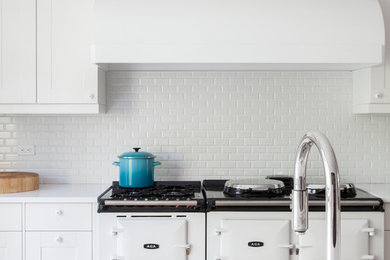 Huge trendy medium tone wood floor eat-in kitchen photo in New York with recessed-panel cabinets, white cabinets, quartz countertops, white backsplash, ceramic backsplash, white appliances, an island and a farmhouse sink