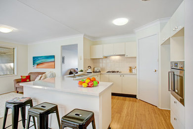Inspiration for a mid-sized beach style u-shaped open plan kitchen in Newcastle - Maitland with a double-bowl sink, flat-panel cabinets, granite benchtops, beige splashback, porcelain splashback, stainless steel appliances, medium hardwood floors and a peninsula.