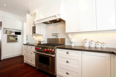 Example of a classic dark wood floor kitchen design in Other with an undermount sink, shaker cabinets, white cabinets, solid surface countertops, white backsplash, glass tile backsplash, stainless steel appliances and an island