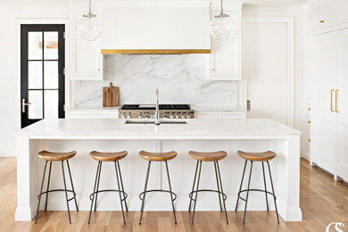 Example of a transitional l-shaped medium tone wood floor kitchen design in Salt Lake City with a drop-in sink, shaker cabinets, white cabinets, marble countertops, marble backsplash, paneled appliances and an island