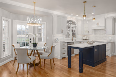 Large transitional u-shaped medium tone wood floor and brown floor eat-in kitchen photo in Other with an undermount sink, recessed-panel cabinets, white cabinets, quartz countertops, white backsplash, ceramic backsplash, stainless steel appliances, an island and white countertops
