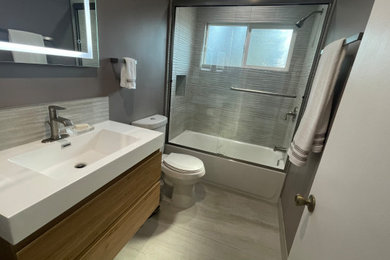 Drop-in bathtub - small modern gray tile and ceramic tile single-sink drop-in bathtub idea in Los Angeles with flat-panel cabinets, brown cabinets, a one-piece toilet, gray walls, quartz countertops and a floating vanity