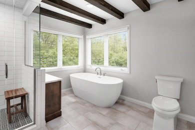 This is an example of a large modern ensuite bathroom in Detroit with shaker cabinets, medium wood cabinets, a freestanding bath, an alcove shower, a two-piece toilet, white tiles, porcelain tiles, beige walls, porcelain flooring, a submerged sink, engineered stone worktops, beige floors, a hinged door, white worktops, a wall niche, double sinks, a freestanding vanity unit and exposed beams.