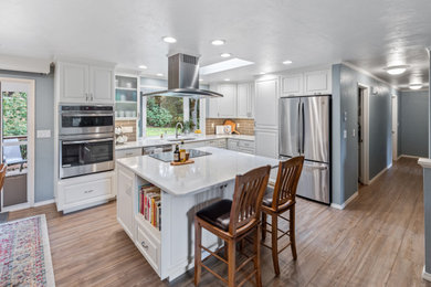 Mid-sized l-shaped vinyl floor and brown floor open concept kitchen photo in Other with an undermount sink, brown backsplash, ceramic backsplash, stainless steel appliances, an island and white countertops