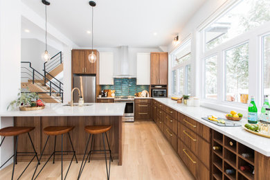 Photo of a large midcentury l-shaped open plan kitchen in Ottawa with a double-bowl sink, recessed-panel cabinets, medium wood cabinets, quartz benchtops, blue splashback, ceramic splashback, stainless steel appliances, light hardwood floors, with island, brown floor and white benchtop.