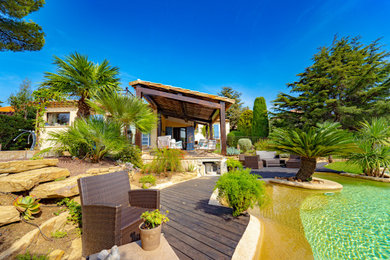 Cette image montre un grand jardin ethnique avec un bassin, une exposition ensoleillée, une terrasse en bois et une clôture en métal.