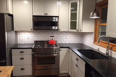 Small minimalist l-shaped dark wood floor eat-in kitchen photo in New York with shaker cabinets, white cabinets, soapstone countertops, white backsplash, subway tile backsplash, stainless steel appliances, an island and an undermount sink