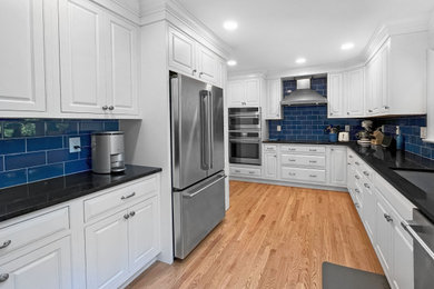 Eat-in kitchen - large coastal u-shaped medium tone wood floor and brown floor eat-in kitchen idea in Philadelphia with an undermount sink, raised-panel cabinets, quartz countertops, blue backsplash, stainless steel appliances and black countertops
